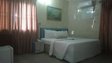 A hotel room with a bed, a nightstand, a telephone, and an air conditioning unit.
