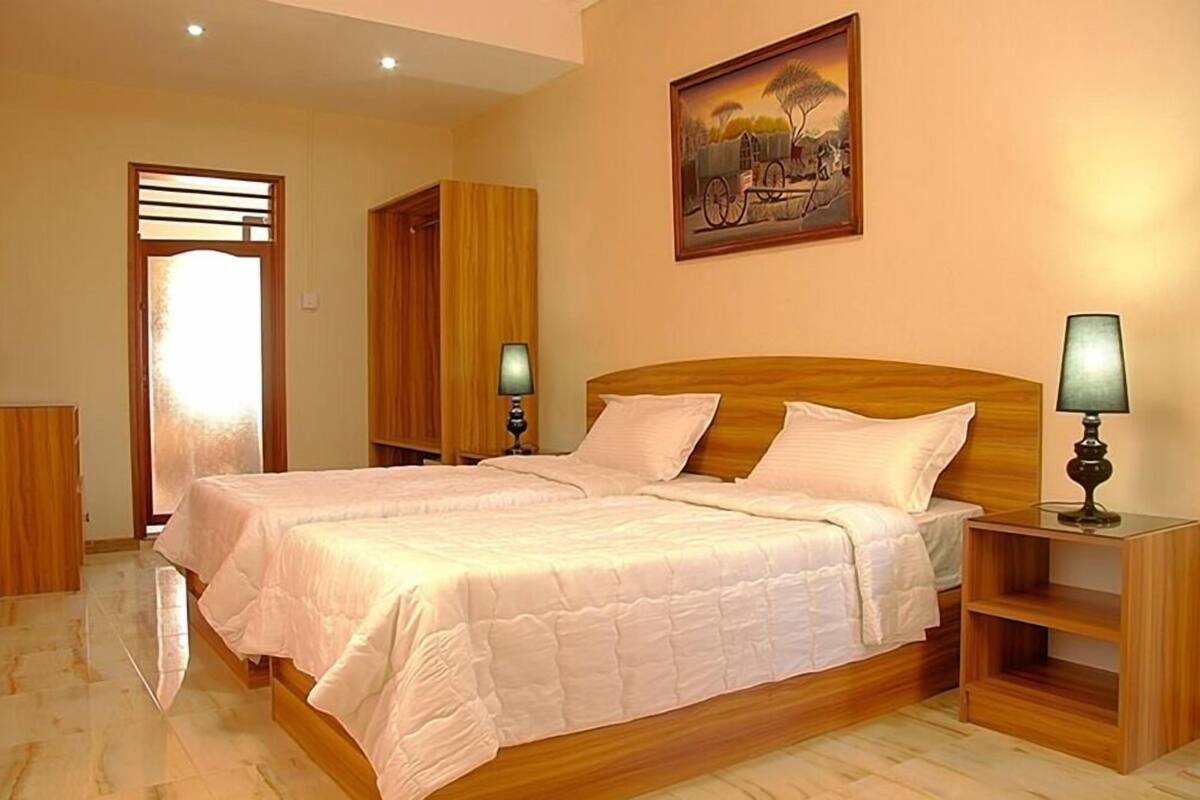 A bedroom with a large bed, wooden headboard, two bedside tables with lamps, a wardrobe, and a painting on the wall.