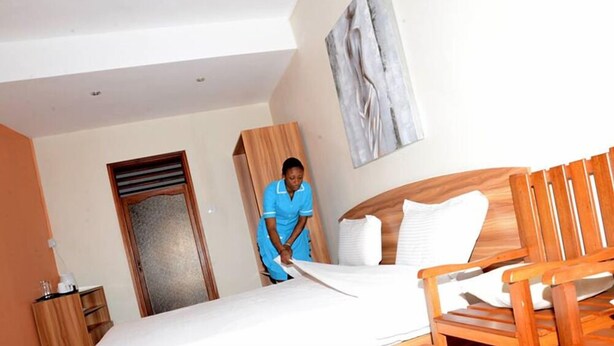 A hotel room with a bed, a wooden chair, a wardrobe, and a painting on the wall. - Auberge le Rajah (Quatre Bornes)
