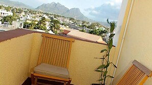 A balcony with two wooden chairs, a potted plant, and a view of a cityscape and mountains. - Auberge le Rajah (Quatre Bornes)