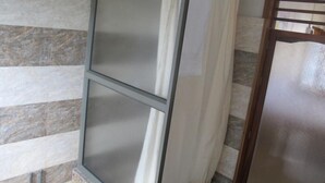 A bathroom with a shower area, tiled walls, and a glass door. - Auberge le Rajah (Quatre Bornes)