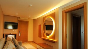 Un salon moderne comprenant un canapé, un téléviseur fixé au mur, un meuble en bois et un miroir doté d’un éclairage intégré.