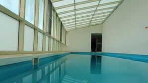 Une piscine intérieure dotée d’un toit en verre, d’une eau d’un bleu cristallin et d’un bord de sécurité bleu.