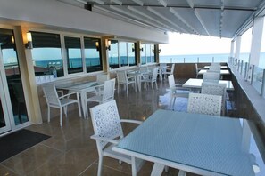 A sunlit outdoor dining area with white wicker furniture and large windows offering ocean views. - Green Suada Hotel (Pazar)