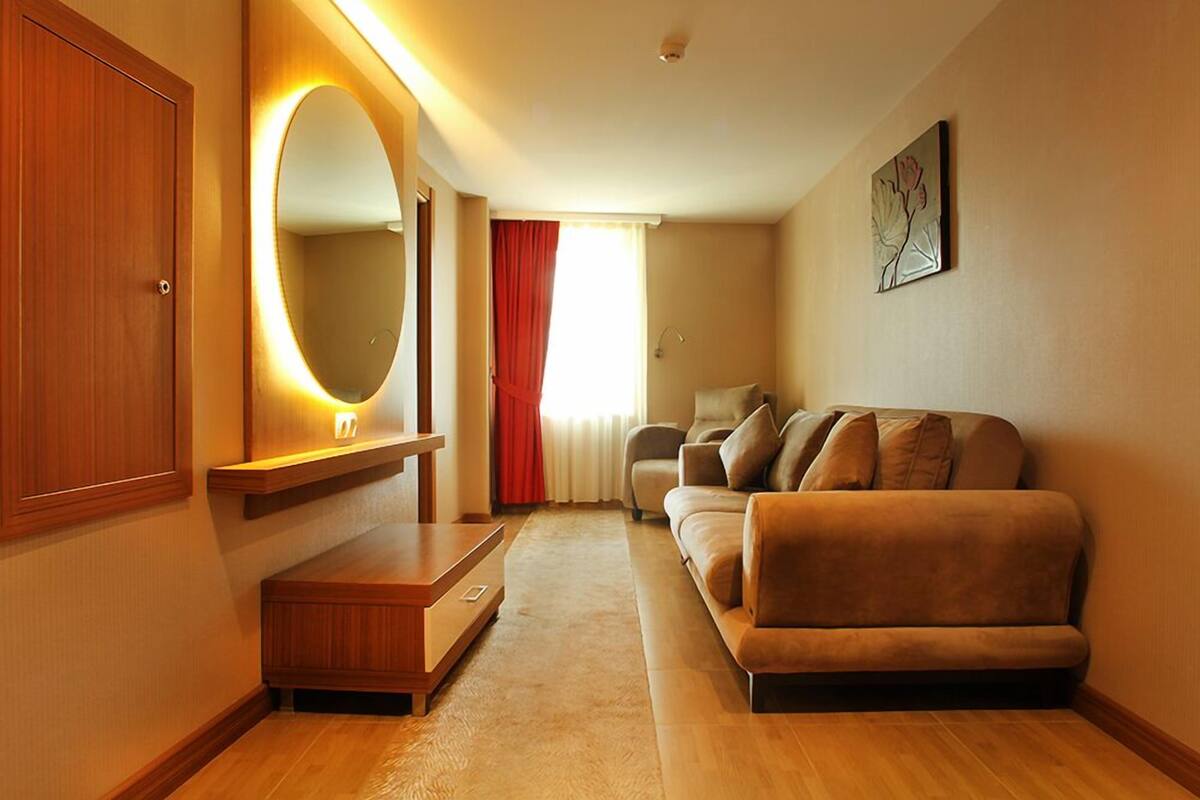 A hotel room with a wooden wardrobe, a sofa, a mirror, and a painting on the wall.
