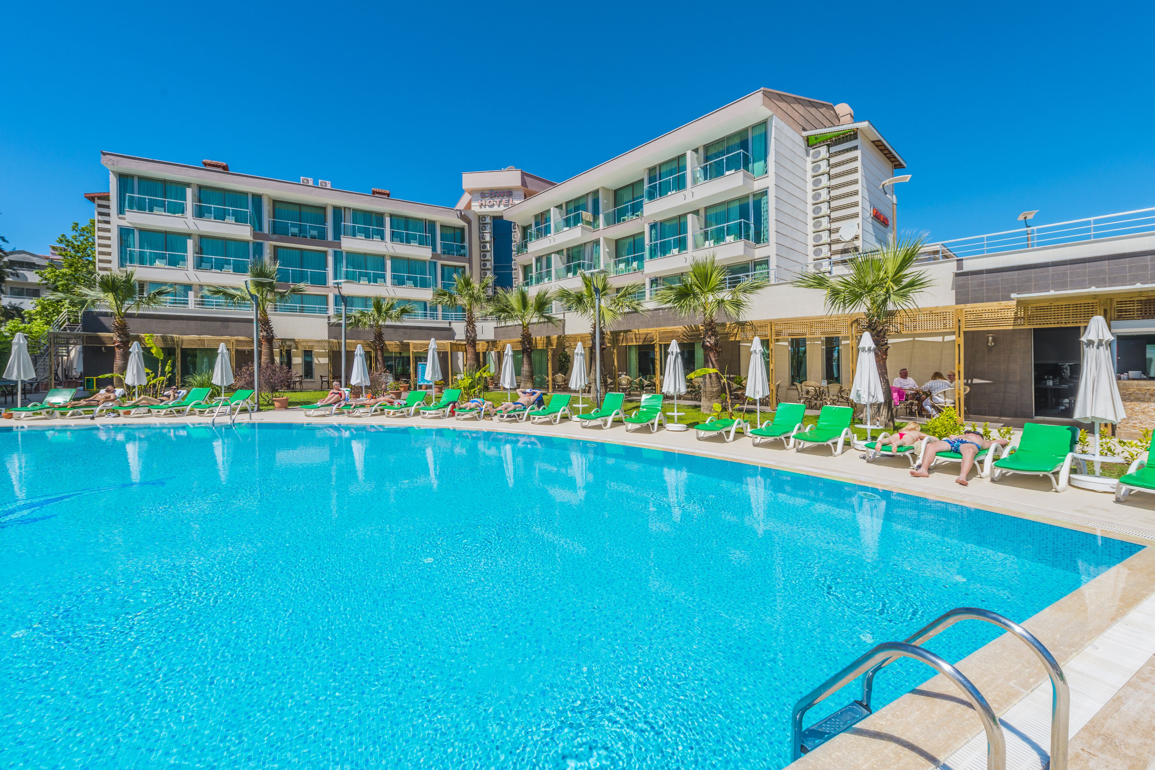 Un hotel con piscina, sillones de jardín verdes y sombrillas.