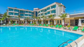 Un hotel con piscina, sillones de jardín verdes y sombrillas.