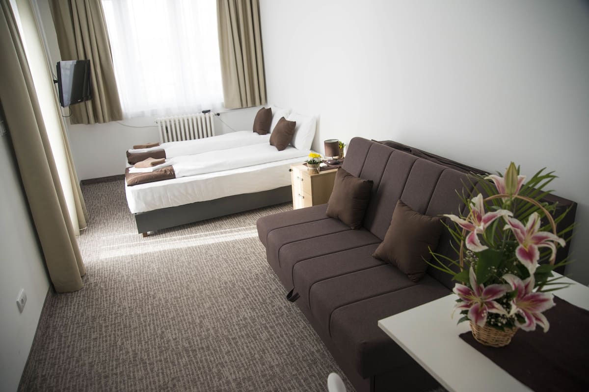 Quarto de hotel com cama, sofá, uma pequena mesa e televisão fixada na parede.