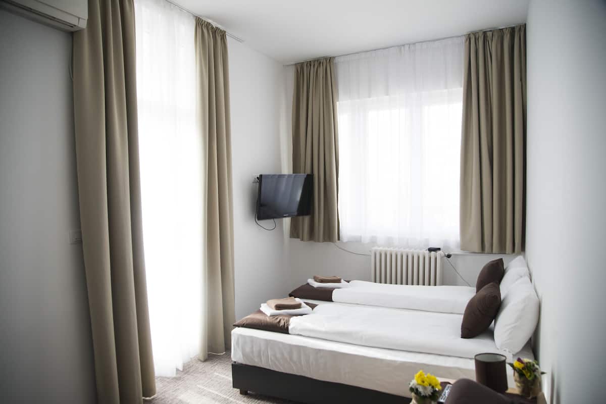 Quarto de hotel com duas camas, uma TV de tela plana na parede e uma janela com cortinas.