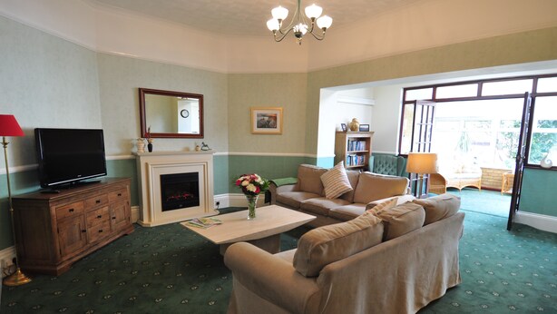 A living room with a sofa, a television, a fireplace, and a bookshelf. - Westbury Lodge (Shanklin)