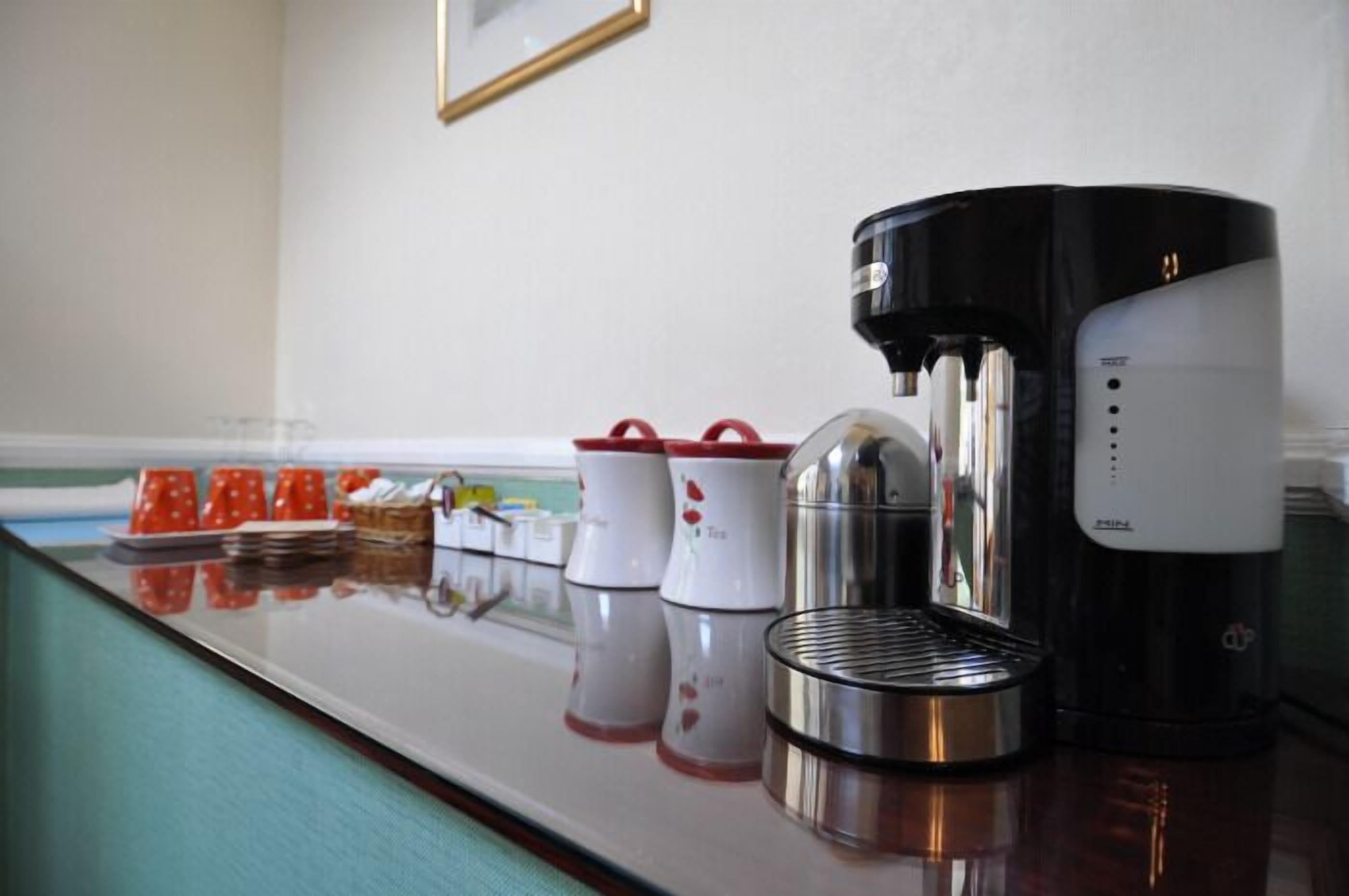 A coffee station with a coffee maker, cups, and a tea kettle on a counter.