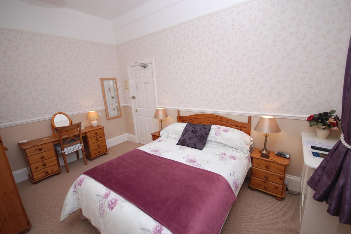 A bedroom with a bed, wooden dresser, nightstands, and a mirror.