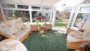 A room with wicker furniture, a green carpet, and large windows offering a view of the outside. - Westbury Lodge (Shanklin)