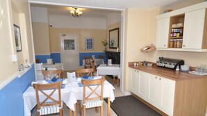 A dining area with a table set for four, a kitchen area with cabinets and a countertop, and a door leading to another room. - Westbury Lodge (Shanklin)