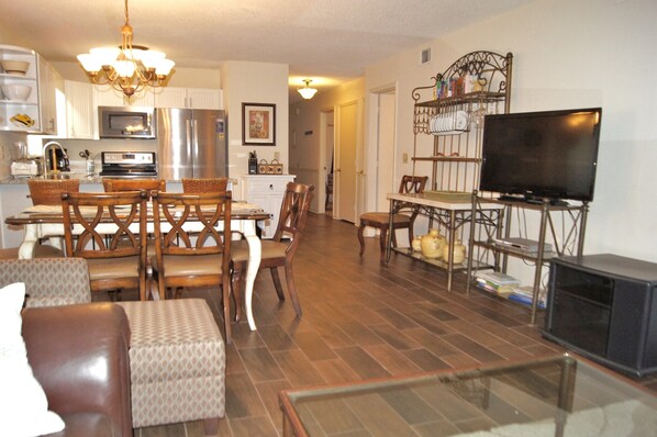 A modern living room with a fireplace, a dining area with a chandelier, and a kitchen with stainless steel appliances. - Sea Cloisters 101d 3 Bedroom Condo by RedAwning (North Myrtle Beach)