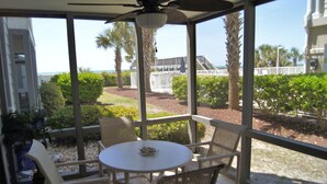 A covered patio with a table and chairs, overlooking a landscaped garden and a view of the beach.