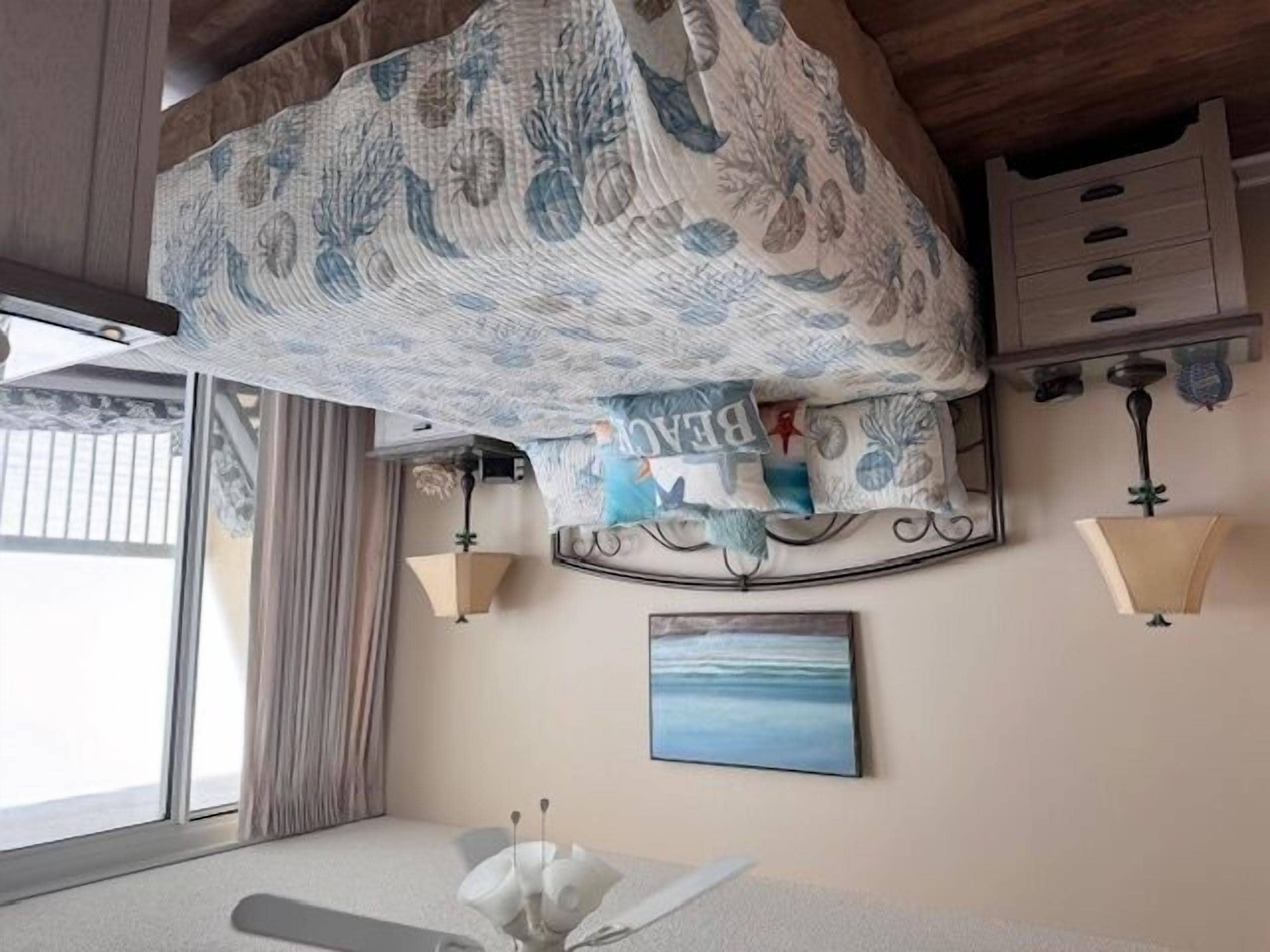 A room with a bed covered by a patterned canopy, a bedside table with a lamp, a wall-mounted shelf, and a painting.