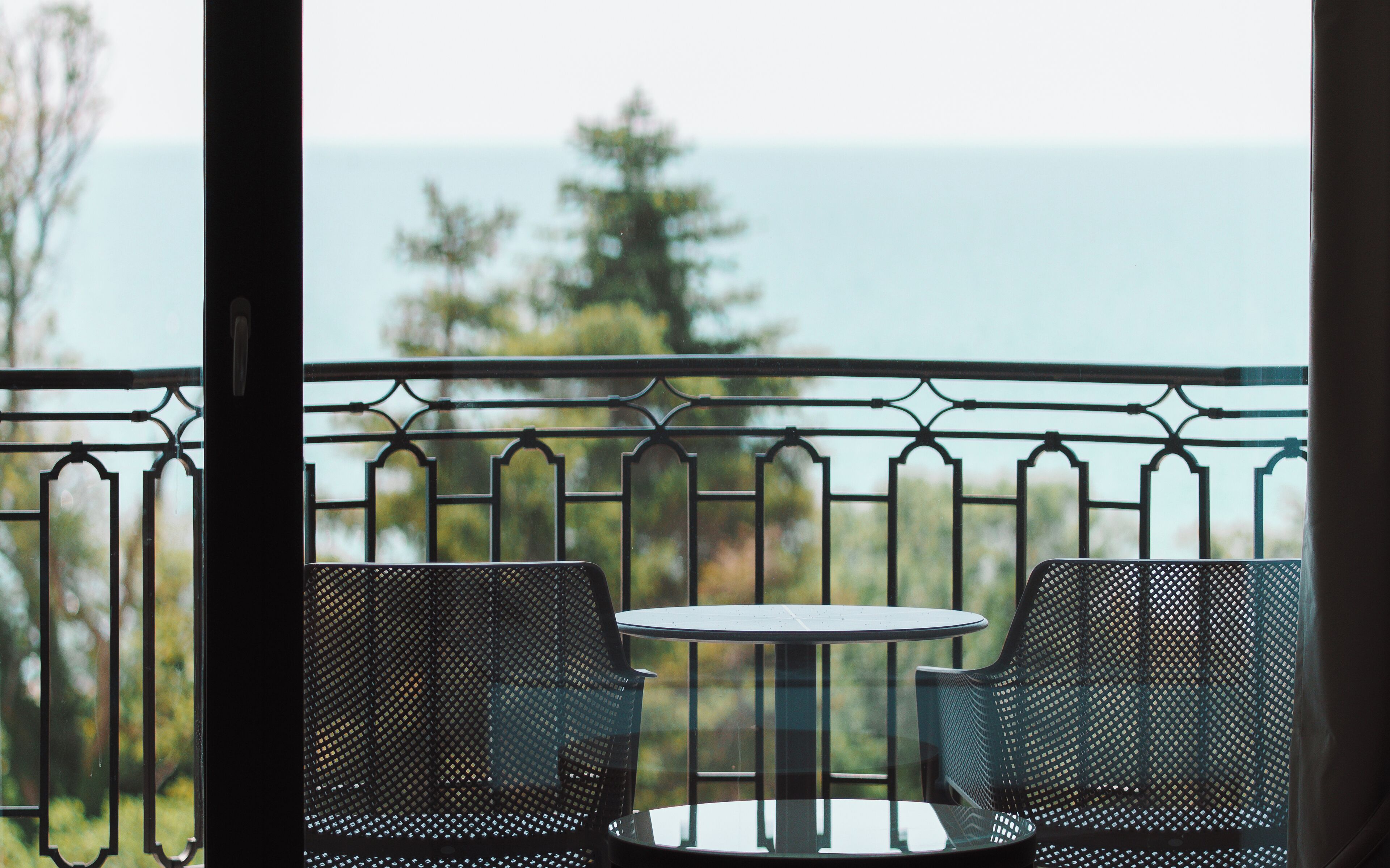 A balcony with two chairs and a small table, overlooking a body of water and trees.