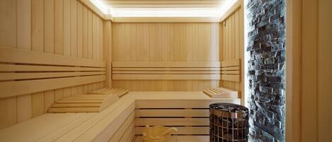 A sauna with wooden benches, a stone wall, and a metal heater.