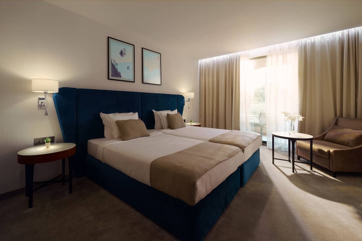 A hotel room with a large bed, a desk, a chair, and a window with curtains.