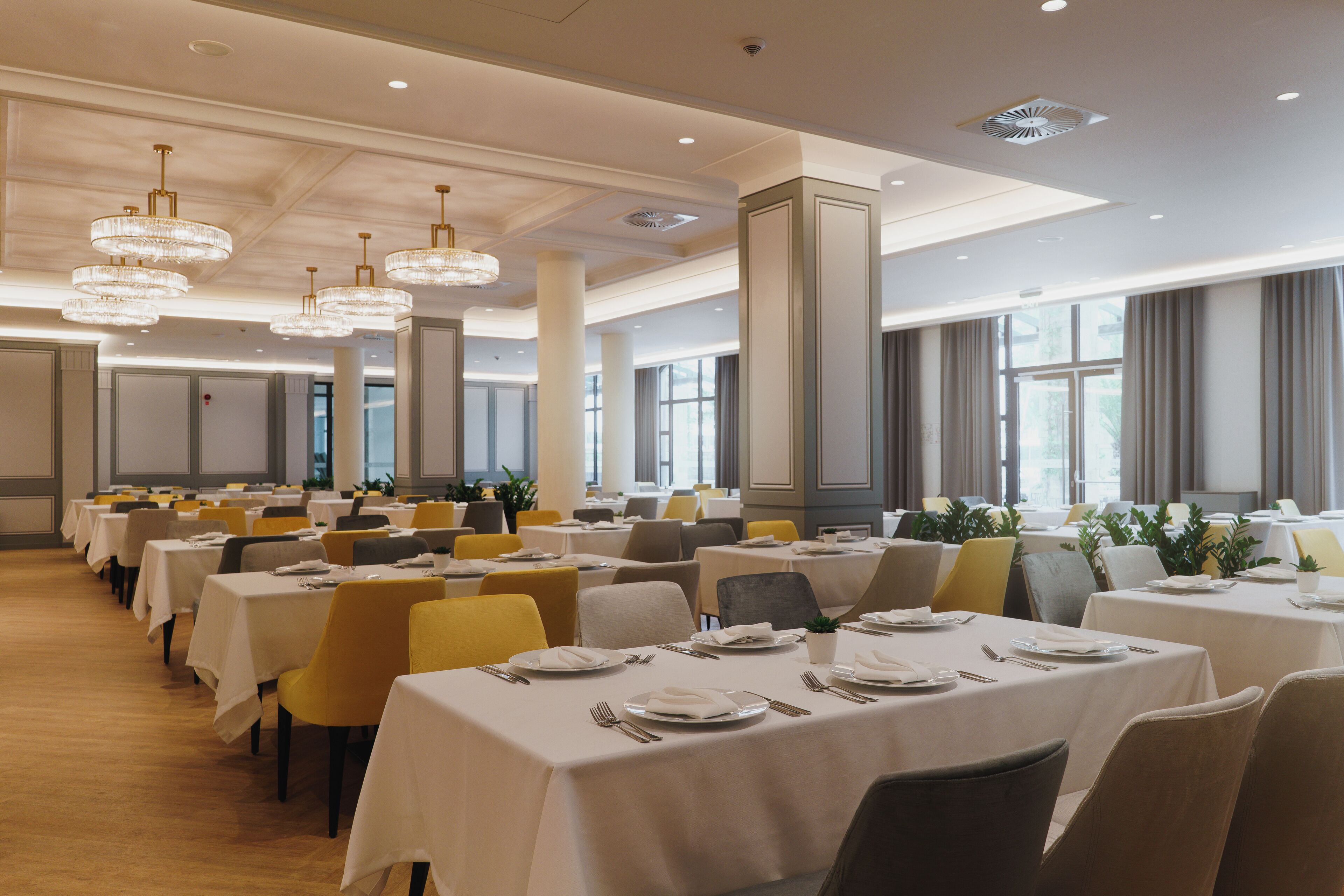 A spacious dining area with multiple tables, chairs, and elegant chandeliers.