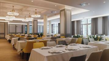 A spacious dining area with multiple tables, chairs, and elegant chandeliers.