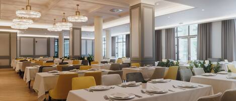 A spacious dining area with multiple tables, chairs, and elegant chandeliers.