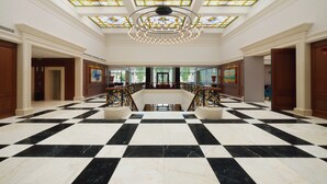 A lobby with a checkered marble floor, a central staircase, and a stained glass ceiling. - Astor Garden Hotel (Varna)
