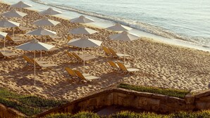 A beach with rows of sun loungers and umbrellas, a stone wall, and the ocean in the background. - Astor Garden Hotel (Varna)