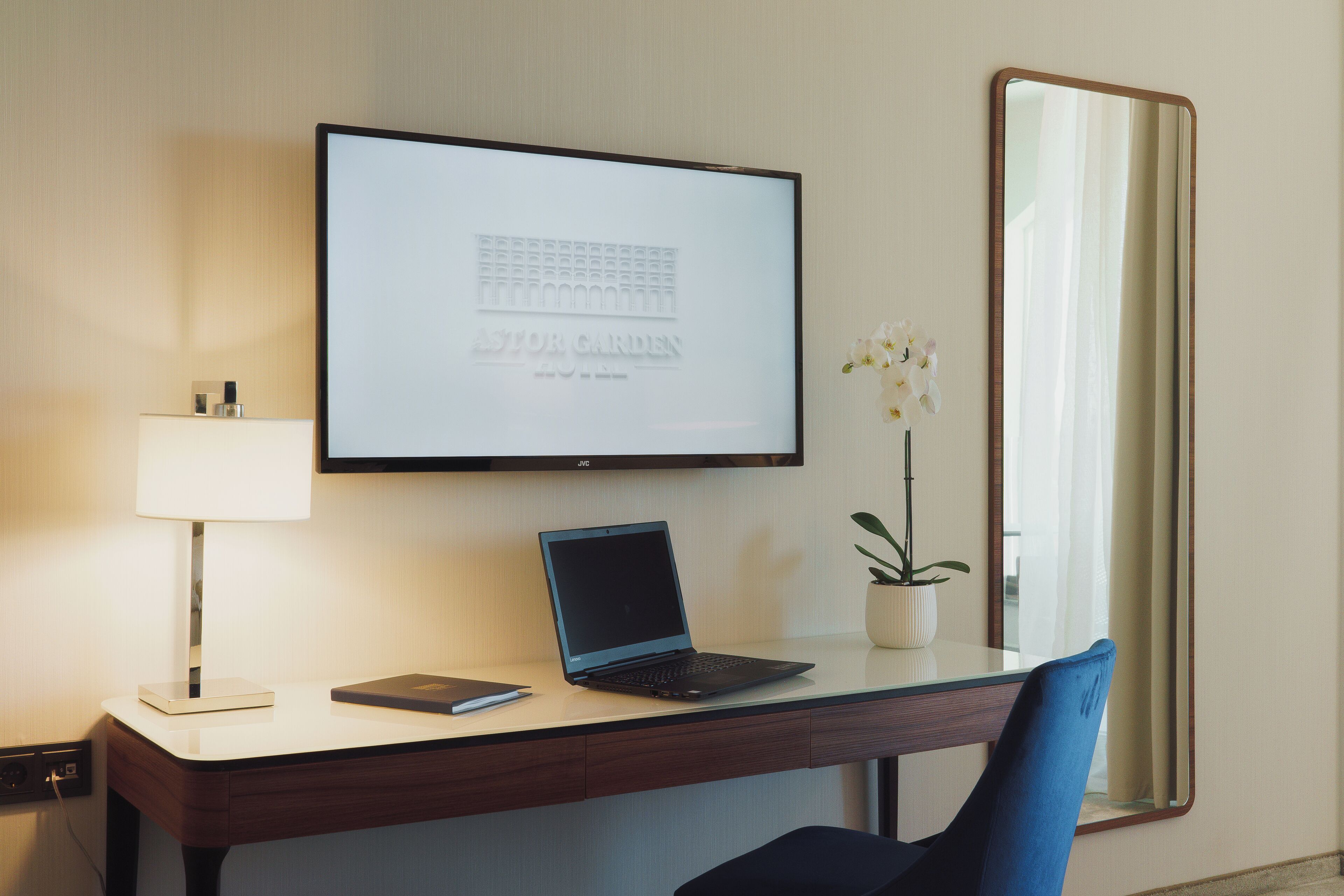 Habitación de hotel con escritorio, laptop, lámpara y un cuadro en la pared.