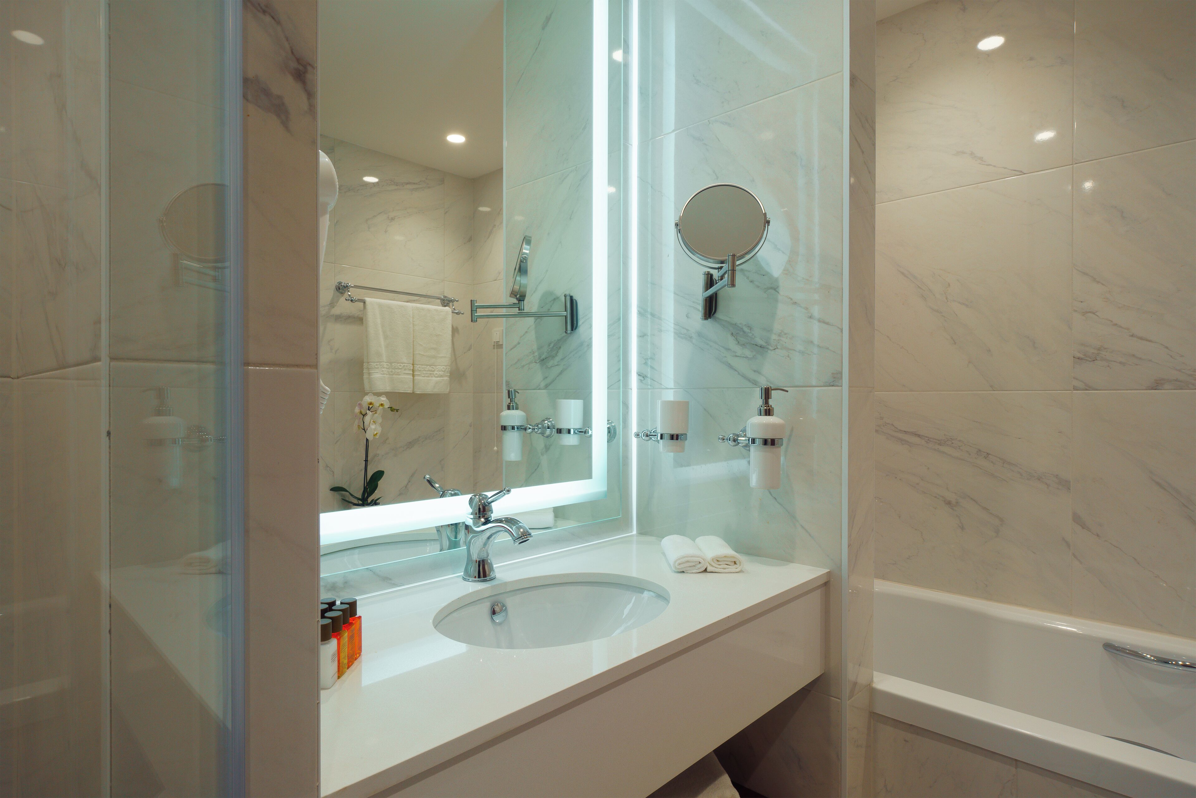 Ein modernes Badezimmer mit einem Glaskonstruktion-Waschtisch, einem großen Spiegel und einer Badewanne.