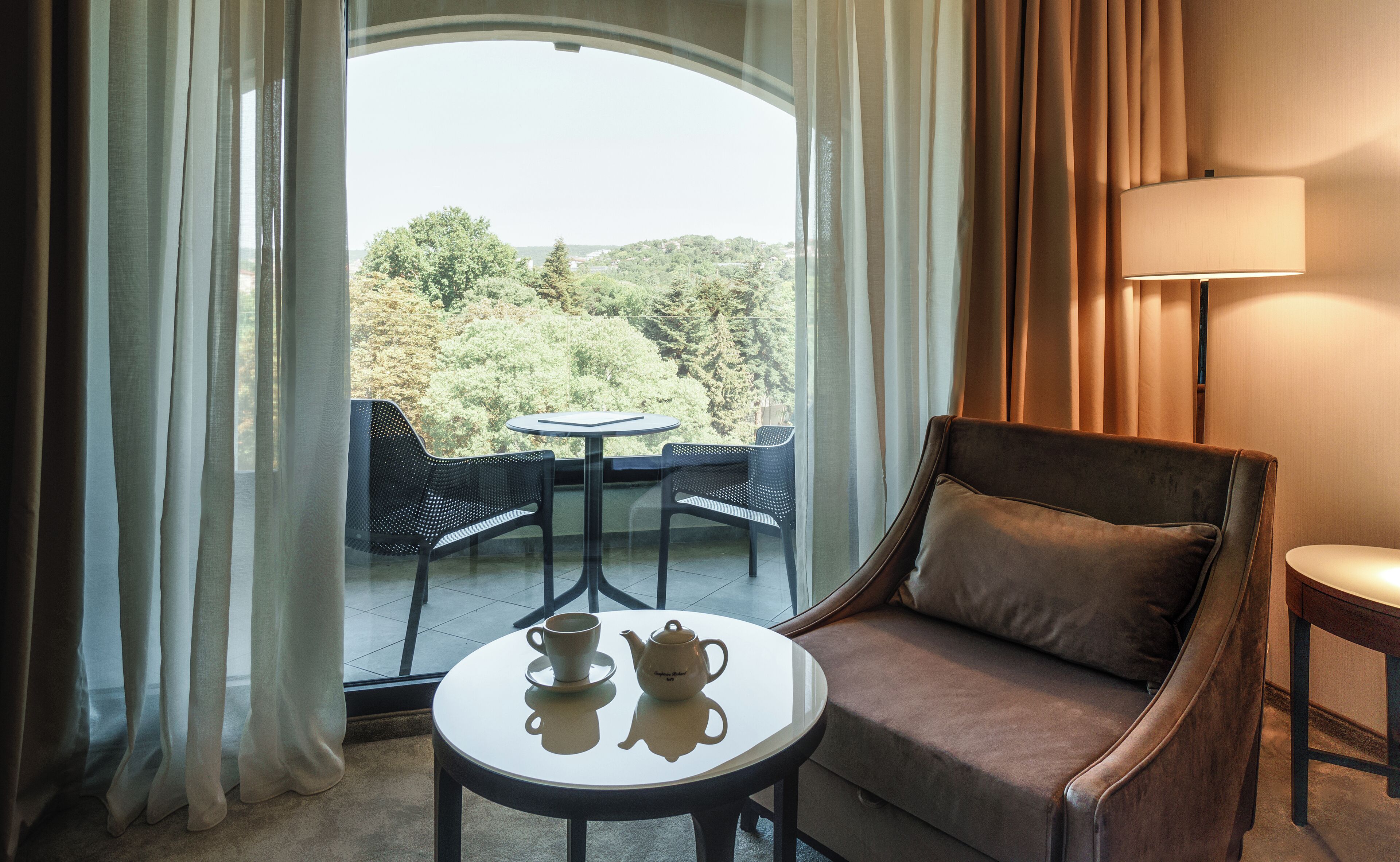 A hotel room with a balcony, a sofa, a table, and a lamp.