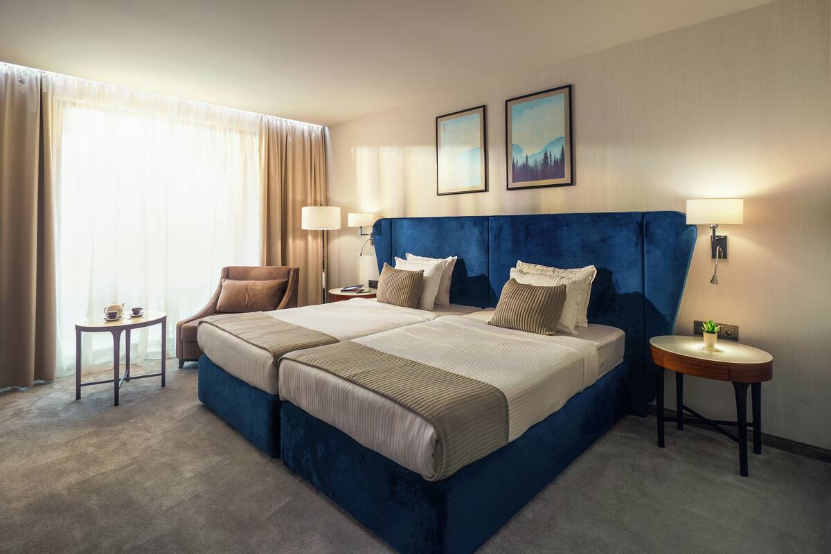 A hotel room with a large bed, two bedside tables, a chair, and a window with curtains.