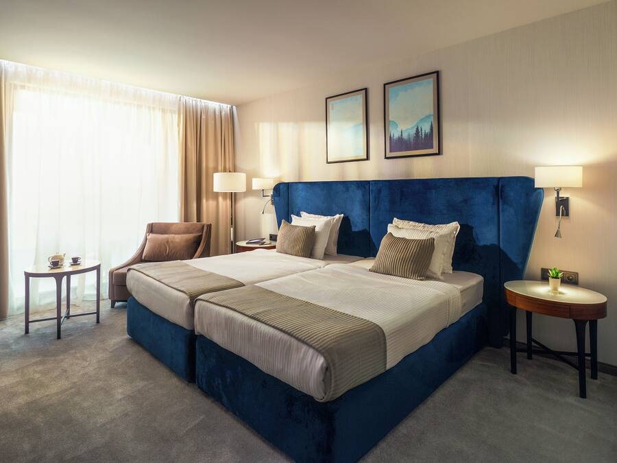 A hotel room with a large bed, two bedside tables, a chair, and a window with curtains.
