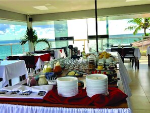 Ein Essbereich mit Meerblick, Tische sind gedeckt mit Tellern, Gläsern und einem Buffet.