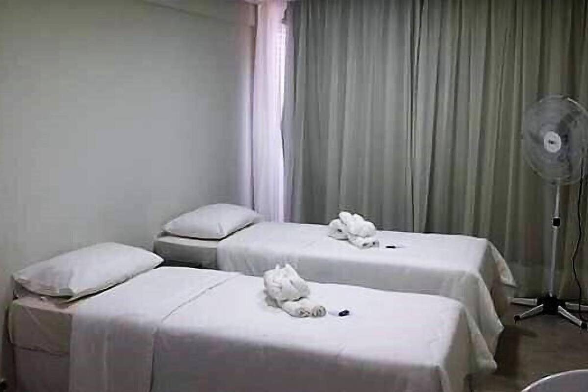 Une chambre avec deux lits, chacun étant équipé d’un oreiller et d’une serviette. On y trouve également un ventilateur sur pied et un rideau.