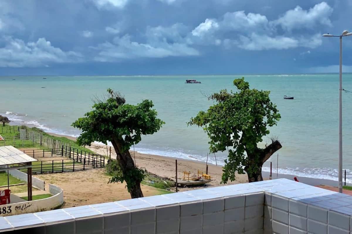 Une vue sur la plage avec une zone délimitée par une clôture, un arbre et un bâtiment portant une enseigne indiquant le numéro « 383 ».