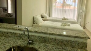 Habitació d'hotel amb taulell de granat, un lavabo, dos llits i un gran finestral amb cortines.