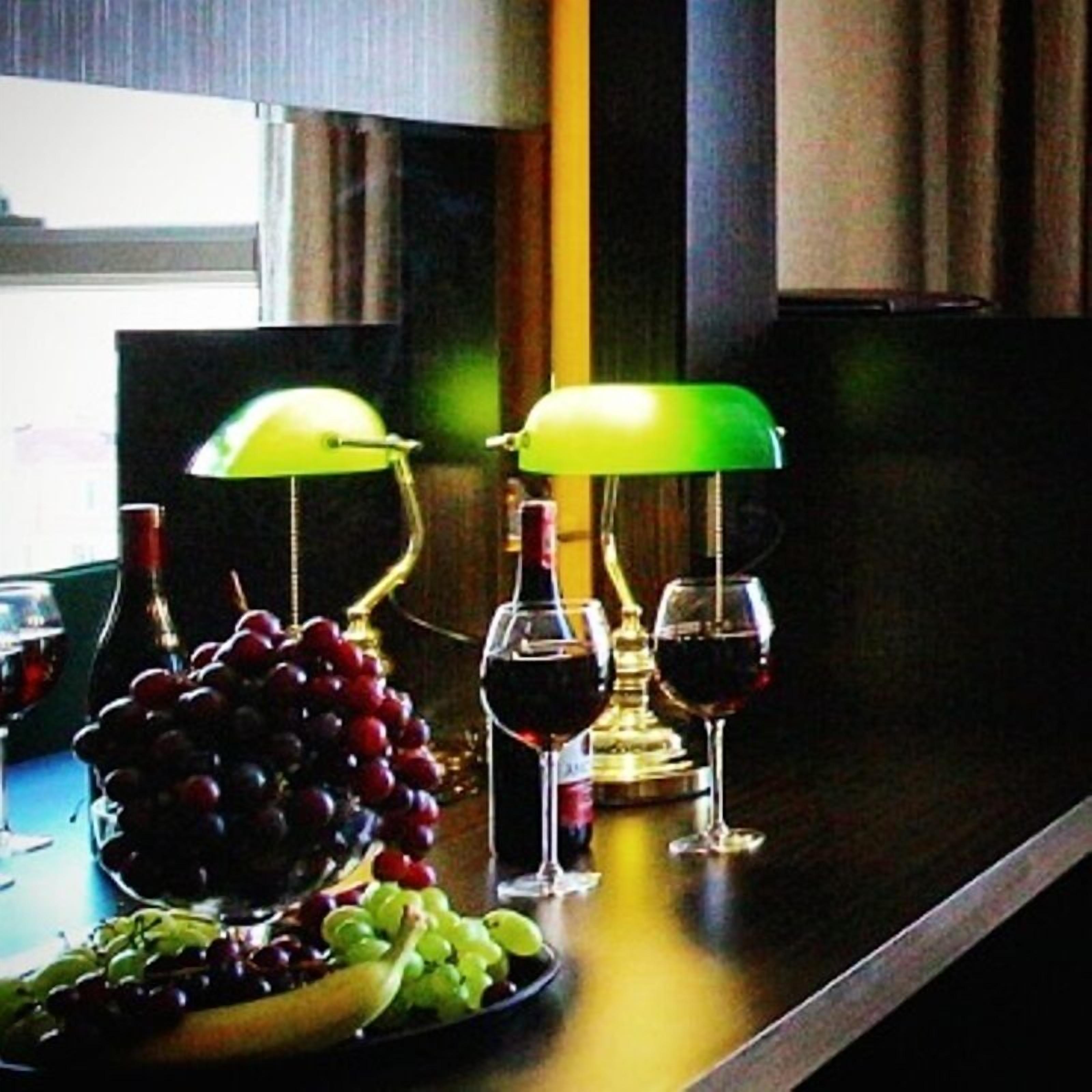 Una mesa con un frutero, dos copas de vino y dos botellas, con dos lámparas a cada lado.