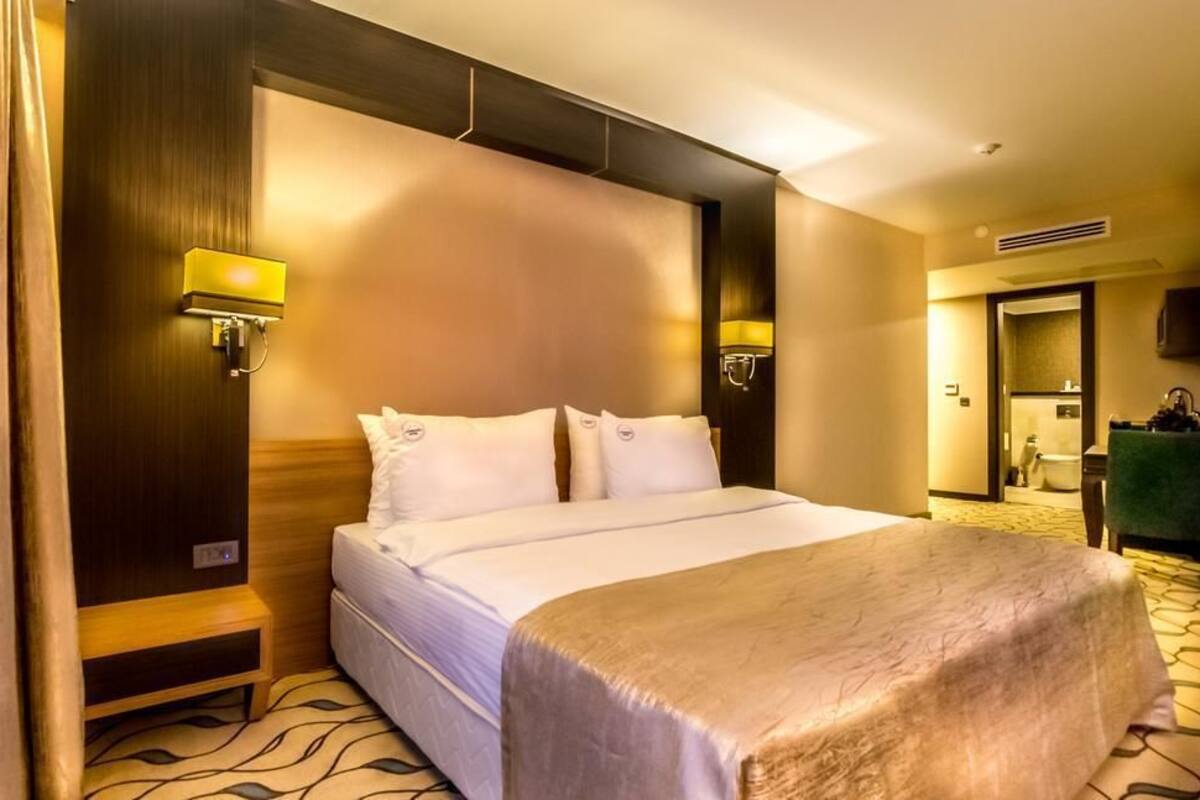 Habitación de hotel con una cama grande, dos lámparas de noche, cabecero de madera y suelo alfombrado.