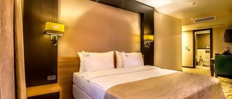 A hotel room with a large bed, two bedside lamps, a wooden headboard, and a carpeted floor.