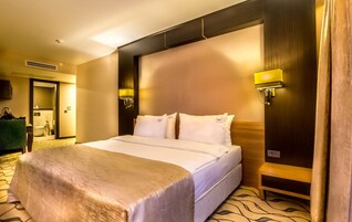 Habitación de hotel con una cama grande, dos lámparas de noche, cabecero y baño visible a través de una puerta abierta.