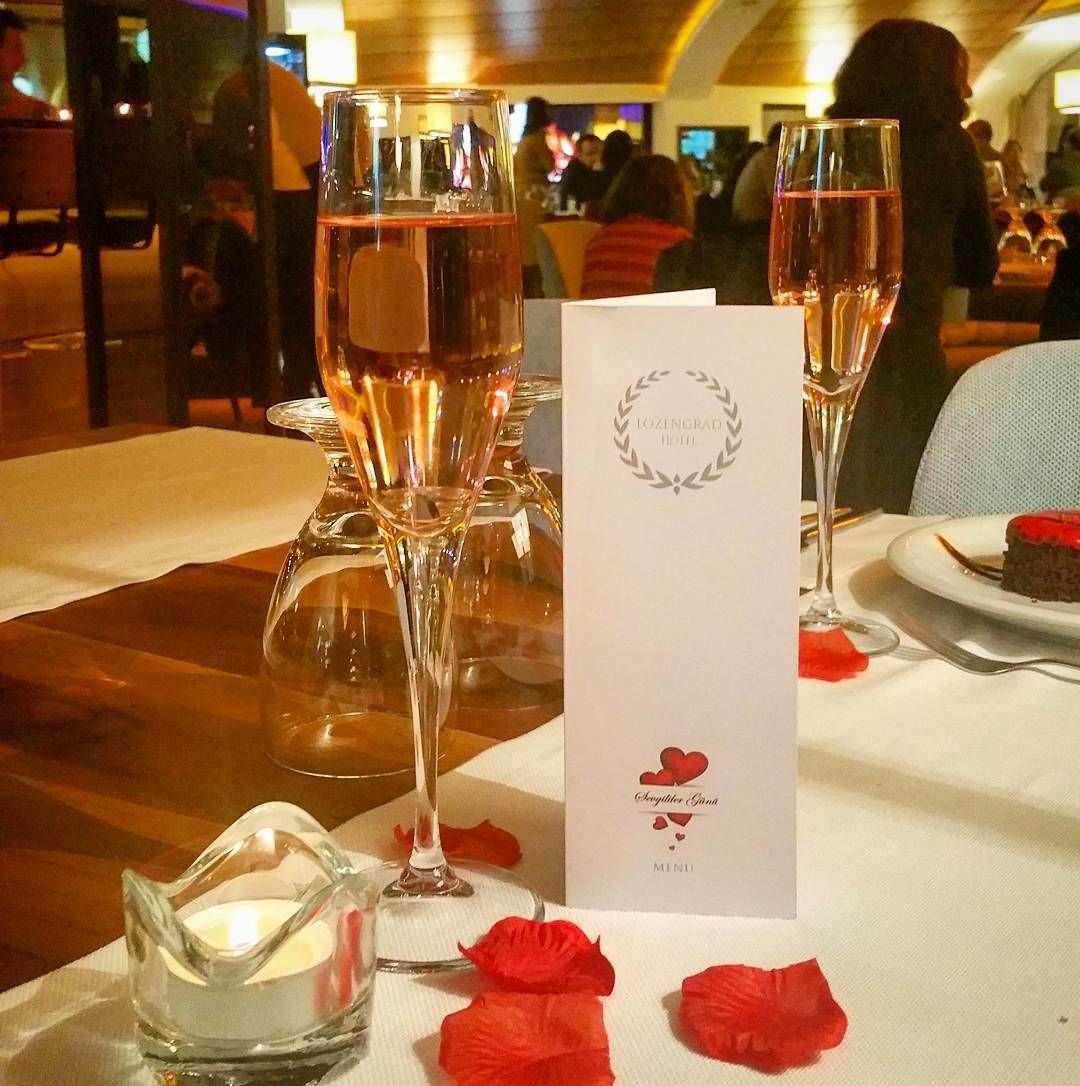 A table set for a meal with a menu, two glasses of wine, and rose petals.