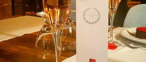 A table set for a meal with a menu, two glasses of wine, and rose petals.