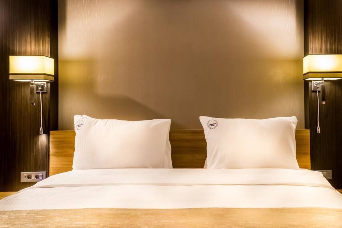 Una habitación de hotel con una cama grande, dos lámparas de noche y un cabecero de madera.