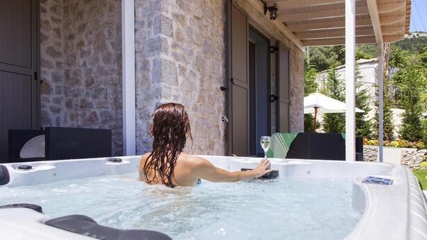 Une personne dans un bain à remous, avec un mur de pierres et du mobilier d’extérieur en arrière-plan.