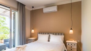 Une chambre d’hôtel avec un lit, deux tables de chevet, un appareil de climatisation et une vue sur l’extérieur, visible à travers une porte vitrée.