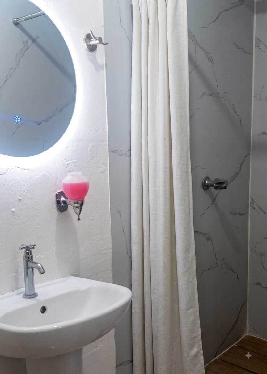 A bathroom with a round mirror, a white sink, a pink soap dispenser, and a shower curtain.