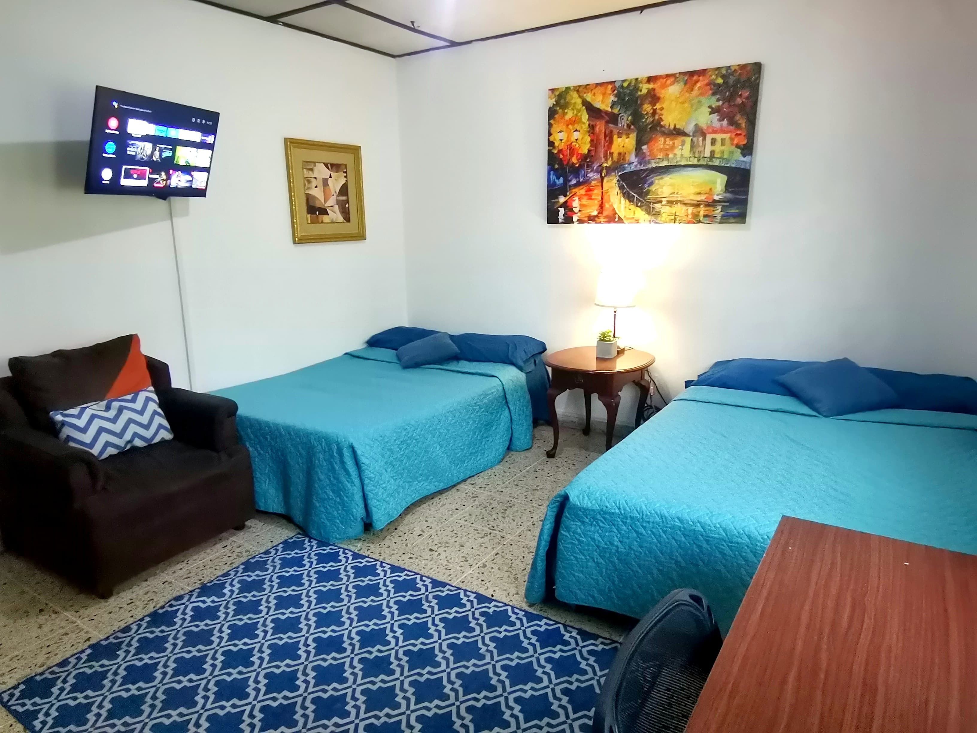 A hotel room with two single beds, a sofa, a TV mounted on the wall, and a painting.
