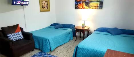 A hotel room with two single beds, a sofa, a TV mounted on the wall, and a painting.